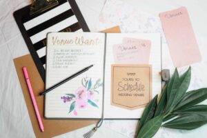 Flat lay of wedding planning materials including a journal, leaves, and stationery.